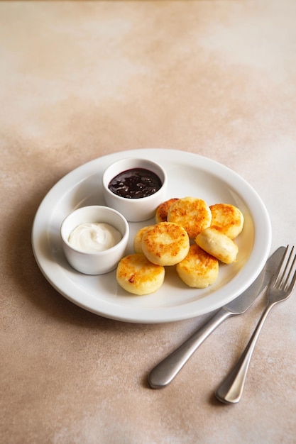 Kwark pannenkoeken syrniki ricotta beignets op witte keramische plaat met zure room en jam Gezond en lekker ochtendontbijt Beige achtergrond Voedsel voor kinderen Oekraïens eten