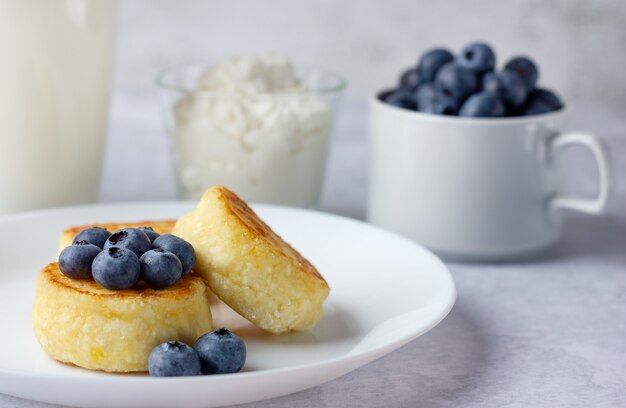 Kwarkpannenkoekjes met bosbessen, zure room en glas melk op steenachtergrond.