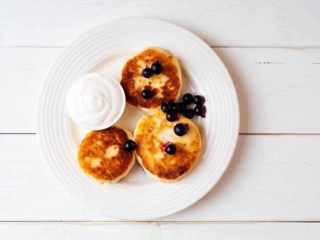 Kwarkpannenkoekjes met zure room en zwarte bes op een witte keramische plaat Ontbijtconcept