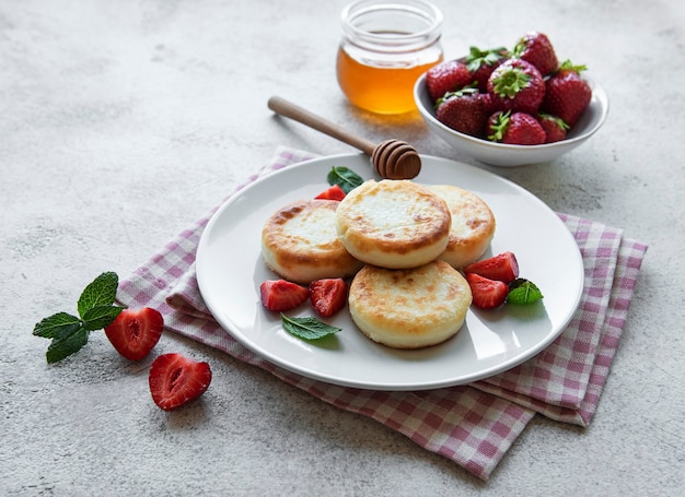 Kwarkpannenkoekjes, ricottabeignets op keramische plaat met verse aardbeien. Gezond en heerlijk ochtendontbijt. Grijze betonnen achtergrond.