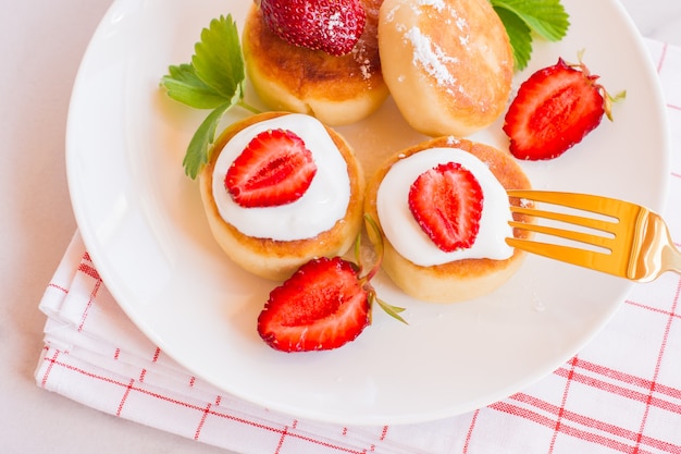 Kwarkpannenkoekjes, syrniki, wrongelbeignets met aardbei. gastronomisch ontbijt. witte achtergrond.