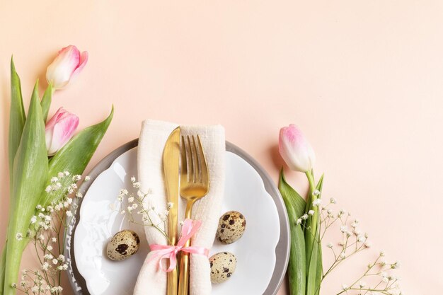 Kwarteleitjes gouden bestek in servet op borden roze tulpen gypsophila op lichte perzik kopieer ruimte