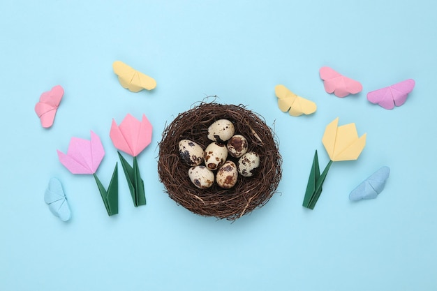 Kwarteleitjes in een nest en origami vlinders tulpen op een blauwe pastel achtergrond Pasen samenstelling Bovenaanzicht