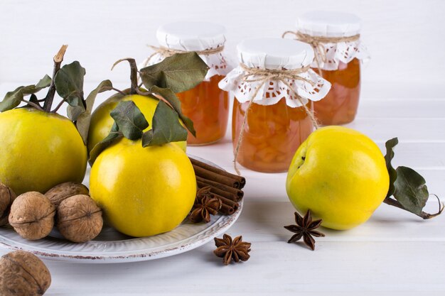 Kweepeerjam in glaskruik en verse kweepeer met bladeren, selectieve nadruk op witte houten lijst.