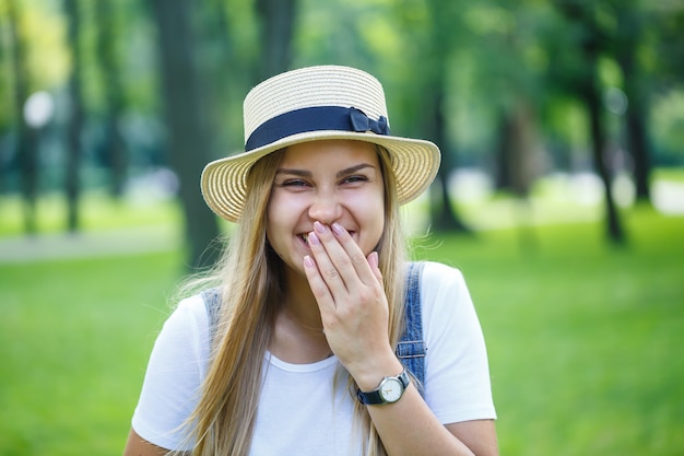 KYIV, UKRAINE - August 2019 young beautiful girl in denim overalls and a light hat walking in the park