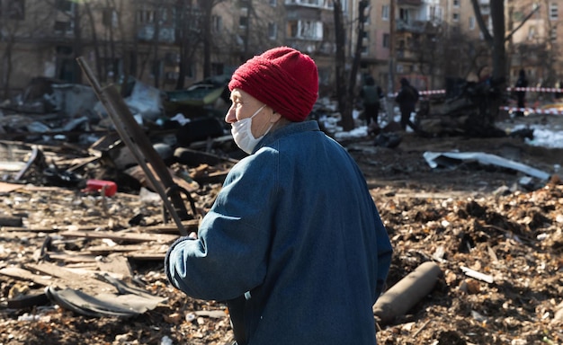 KYIV UKRAINE Mar 18 2022 War in Ukraine Damaged residential buildings in the aftermath of a shelling in Kyiv An elderly woman in a medical mask among the rubble of a destroyed house