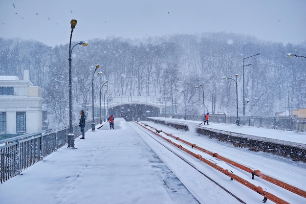 Kyiv ukraine march 4 2018 dnipro metro station platform with\
passengers waiting train and workers cleaning snow during snowfall\
kiev