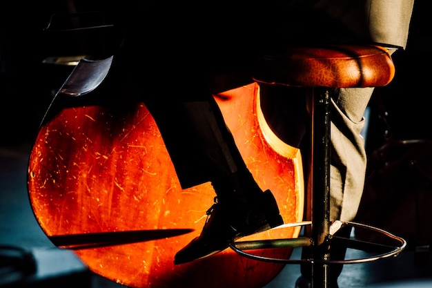 Laag gedeelte van een man die cello speelt terwijl hij op een kruk zit
