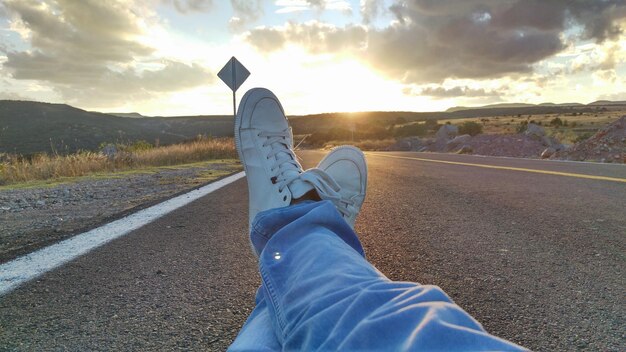 Laag gedeelte van een persoon op de weg tegen de hemel tijdens zonsondergang