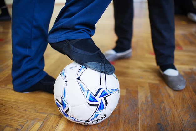 Foto laag gedeelte van het been van een man met een voetbal terwijl hij op een houten vloer staat