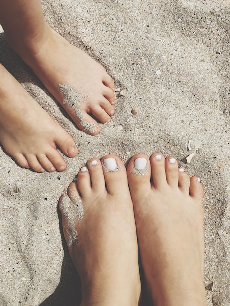 Foto laag gedeelte van moeder en dochter die op het zand op het strand staan