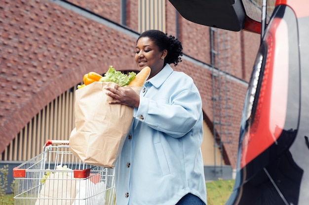 Laag hoekportret van een glimlachende vrouw die een boodschappentas in de kofferbak stopt na het winkelen bij de supermarkt