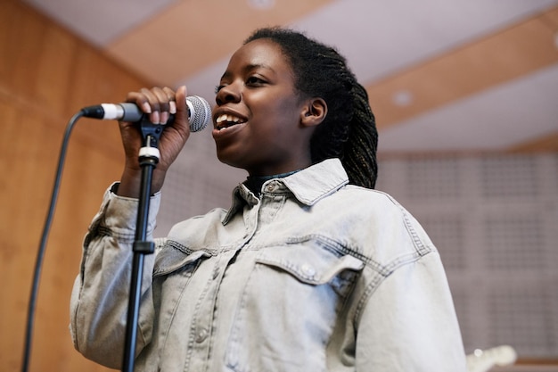 Laag hoekportret van jonge zwarte vrouw die naar de microfoon zingt tijdens het opnemen van muziek of het repeteren in