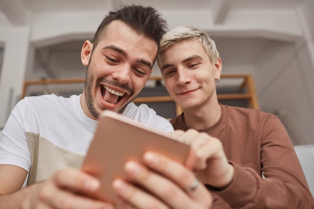 Laag hoekportret van twee jonge mannen die lachen terwijl ze naar het tabletscherm in het interieur kijken