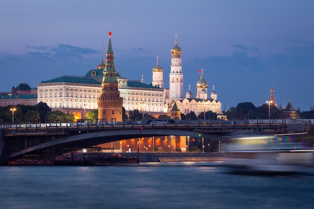 Laag uitzicht op het Kremlin op het blauwe uur, een brug ervoor en een wazige boot op de rivier