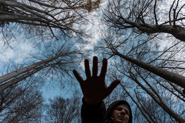 Foto laaghoekbeeld van een man die een stopteken tegen bomen in het bos geeft