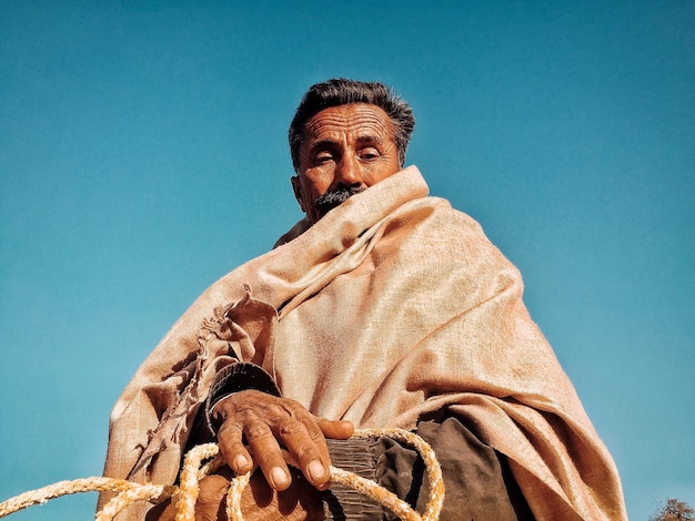 Laaghoekportret van een man die een sjaal draagt tegen een heldere blauwe lucht