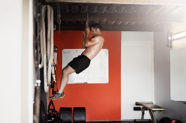 Laat je doelen nooit los Full-length shot van een knappe en gespierde jongeman die pullups doet met een ketting in de sportschool