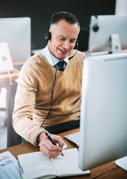 Laat me dat opschrijven Bijgesneden opname van een knappe, volwassen mannelijke telefoniste die aan zijn bureau werkt