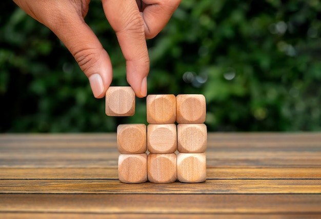 Laatste stuk houten kubus blok in de hand het opleggen van houten cubus als puzzels stapelen rangschikken voltooid op tafel en groene plant achtergrond oplossing oplossen van probleem zakelijk doel en succesplan concepten