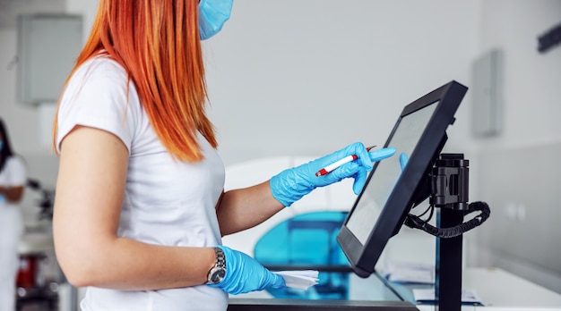 Lab assistant standing in laboratory and using computer for entering data for covid-19 positive patients.