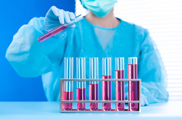 Uniforme da assistente di laboratorio con guanti maschera che tengono una provetta con un campione di ricerca di laboratorio scientifico mentre si analizza lo sviluppo sulla chimica biologica come la crescita del grafico aumenta lo spazio di copia delle entrate dell'investimento