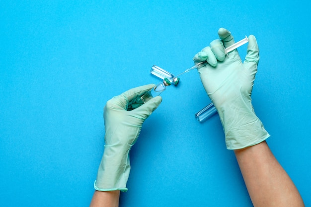 Lab technician assistant or doctor wearing rubber or latex gloves holding an ampoule with medicine or vaccine and syringe