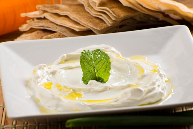 Labneh, toum, hommos, chancliche, garlic paste, arab food on white plate with orange fabric on background