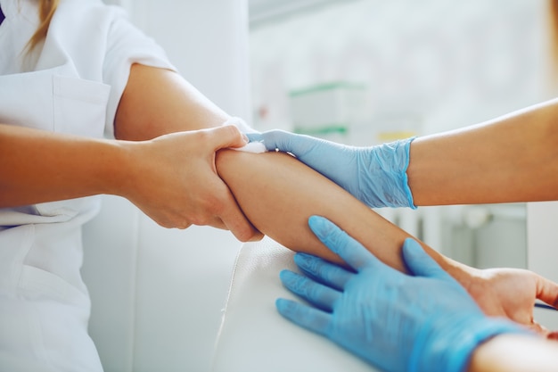 laboratoriumassistent die absorberend katoen op de arm van de patiënt legt na het nemen van bloedmonster.