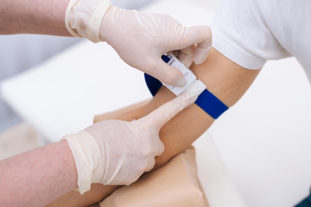 Laboratory assistant preparing patient to do a blood analysis. Nurse tightening the medical tourniquet on arm before taking blood sample. Concept of healthcare and medicine.