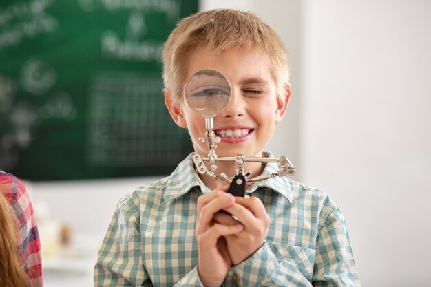 Laboratory equipment. cheerful nice boy looking into the magnifying glass while being in the school lab