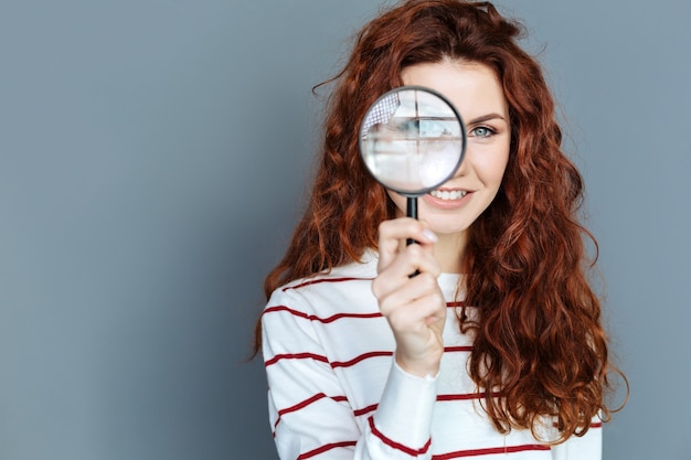 Photo laboratory equipment. close up of magnifying glass being in hands of a cheerful smart red haired woman while doing a research