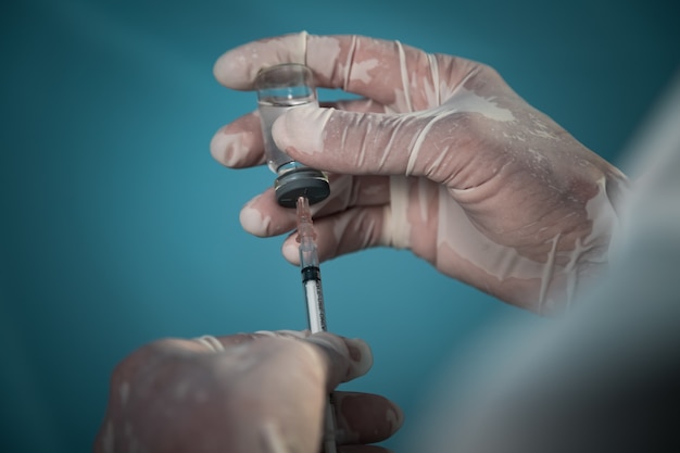 Laboratory researcher scientist wearing PPE suit, mask and gloves, draws COVID-19 vaccine liquid into the syringe. Fighting the coronavirus pandemic.