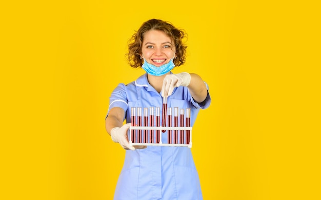 Laboratory researcher. woman wears protective mask. making lab\
experiment. test your blood. scientist in face mask and gloves\
holding test tube with red substance. investigator checking test\
tubes.