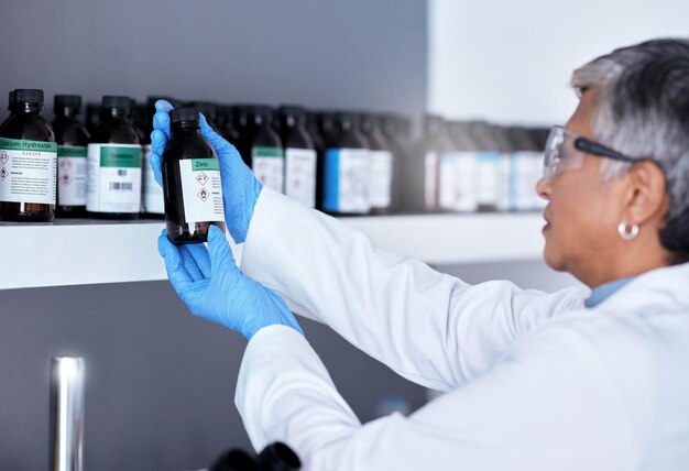 Laboratory science and woman with bottle from shelf to check medical research information Healthcare medicine and innovation in manufacturing of vaccine or prescription drugs with senior scientist