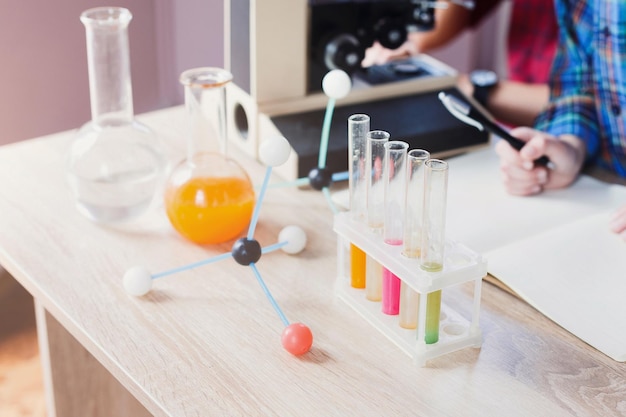 Laboratory test tubes, flasks with colored liquids and molecualar structure model on the desk in science class. Science, chemistry and biology concept