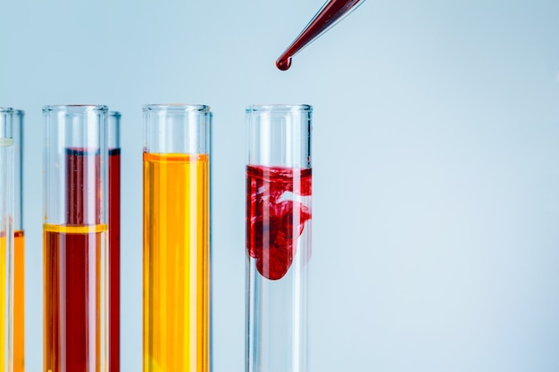 Laboratory test tubes with red and yellow liquids on light blue background