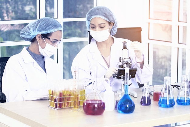 Photo laboratory two woman scientists conduct experiments chief research scientist adjusts specimen in a petri dish and looks on it into microscope