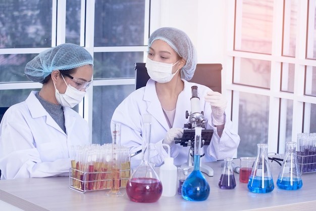 Photo laboratory two woman scientists conduct experiments chief research scientist adjusts specimen in a petri dish and looks on it into microscope