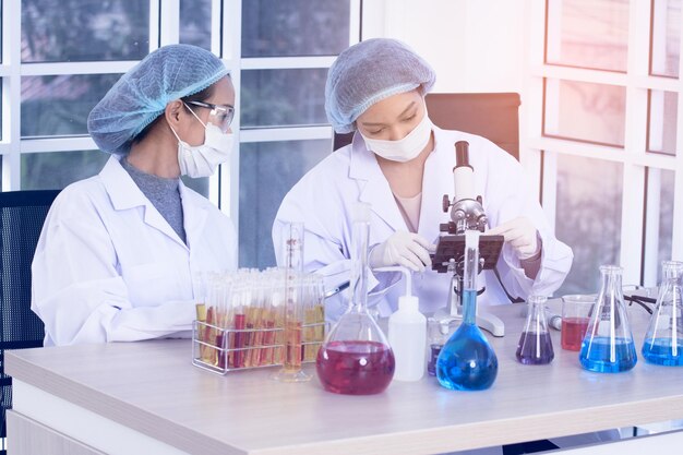 Photo laboratory two woman scientists conduct experiments chief research scientist adjusts specimen in a petri dish and looks on it into microscope