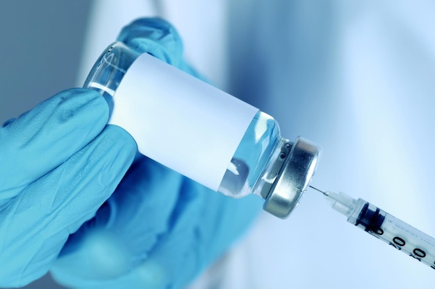 Laboratory worker filling syringe with medication from glass vial closeup