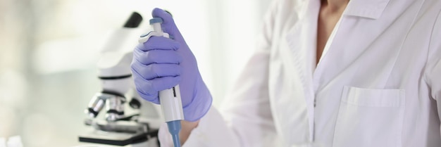 Laboratory worker in uniform does professional research of liquid sample against microscope