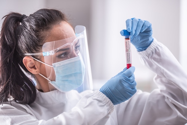 Laboratory worker wearing protective equipment examines an ampule with a Covid-19 test.