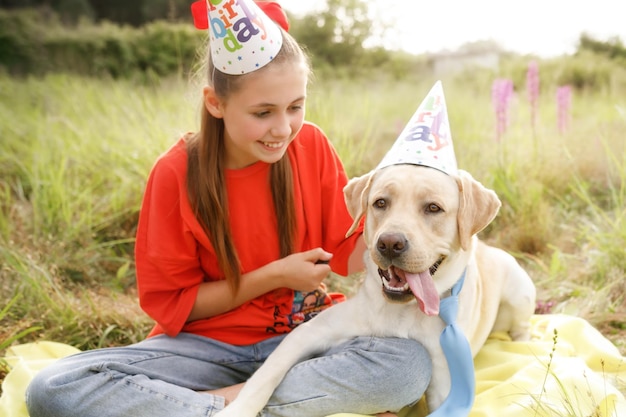 Labrador viert zijn verjaardag met zijn minnares in de natuur in feestelijke petten en een blauwe stropdas soft focus