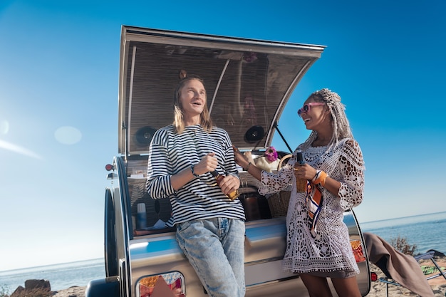 Lach en bier. Stijlvol modern stel dat zich ontspannen voelt terwijl ze lachen en bier drinken in de buurt van hun stacaravan