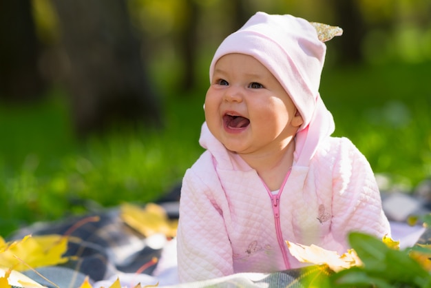 Lachend babymeisje met een brede stralende glimlach spelen op een deken op het gras in een herfstpark in een openhartig portret