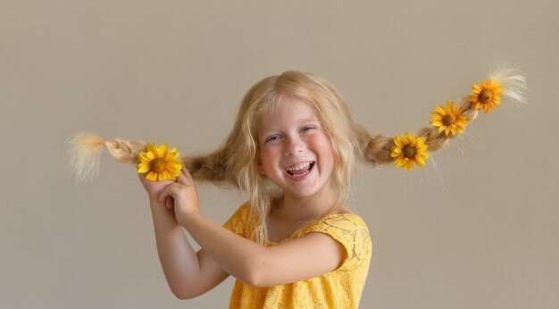 Lachend blond meisje met bloemen in haar vlechten