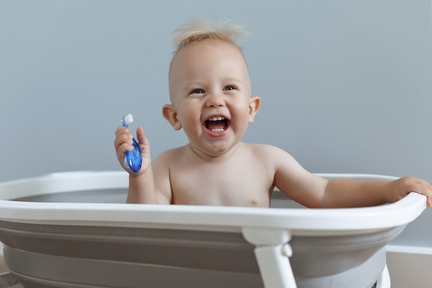 Foto lachend klein kind poetst zijn tanden terwijl hij in de badkamer zit