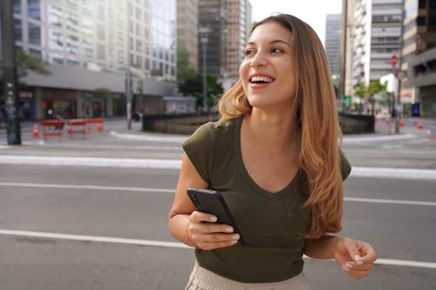 Lachend meisje dat mobiele telefoon vasthoudt en naar de zijkant kijkt in de lege metropoollaan