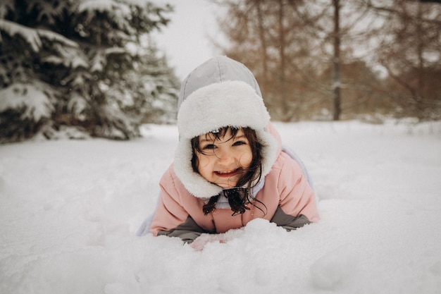 Lachend meisje in een warm winterpak ligt in diepe sneeuw.